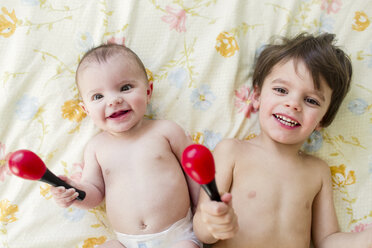 Zwei Kinder, ein Junge und ein kleines Mädchen, liegen auf einem Bett und halten Maracas. - MINF05351