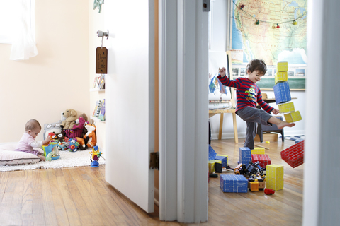 Zwei Kinder in verschiedenen Räumen, ein kleines Mädchen, das mit Spielzeug spielt, und ein Junge, der einen Turm aus Bauklötzen umstößt., lizenzfreies Stockfoto