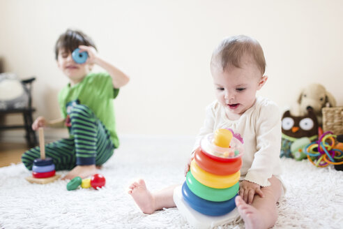 Zwei Kinder, ein Junge und ein kleines Mädchen, sitzen auf einem Teppich und spielen mit Spielzeug. - MINF05357