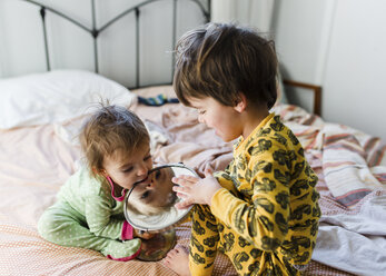 Two children sitting on a bed, a boy and his baby sister chewing a mirror. - MINF05370