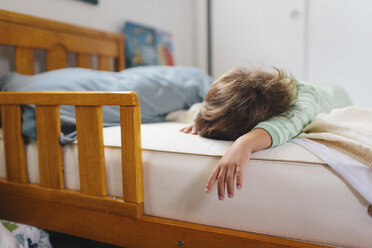 Junge mit braunem Haar und gestreiftem grünem Strampler liegt auf dem Bauch auf einem Bett und schläft. - MINF05378