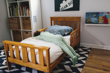 Kleiner Junge mit gestreiftem grünem Strampler auf dem Bauch liegend auf einem Bett. - MINF05379