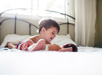 Junge mit braunem Haar und kleinem Baby auf einem Bett liegend. - MINF05380