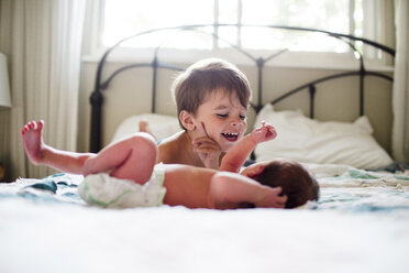Junge mit braunem Haar und kleinem Baby auf einem Bett liegend. - MINF05381