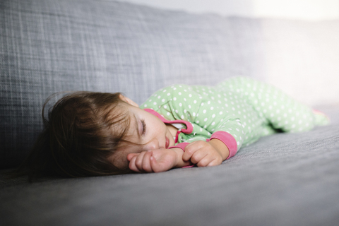 Junges Mädchen in grünem Schlafanzug liegt auf der Seite auf einem Sofa und schläft., lizenzfreies Stockfoto