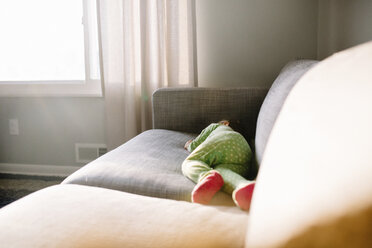 Junges Mädchen in grünem Schlafanzug liegt auf der Seite auf einem Sofa. - MINF05394