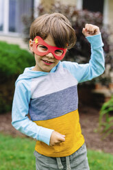 Young boy with brown hair wearing superhero mask standing outdoors, arm raised, looking at camera. - MINF05410
