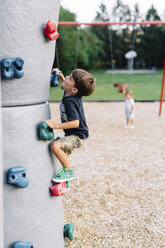 Junge mit braunem Haar, der auf einem Spielplatz eine Kletterwand hochklettert. - MINF05420