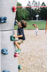 Young boy with brown hair climbing up a climbing wall in a playground. - MINF05420