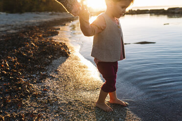 Junges Mädchen steht bei Sonnenuntergang an einem Sandstrand und taucht ihre Zehen ins Meer. - MINF05433