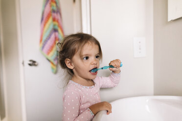 Young girl with brown hair standing at a bathroom sink, brushing her teeth. - MINF05437