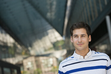 Outdoors in the city. In a public space. Business people on the move. A young man in a striped sweater looking into the distance. - MINF05456