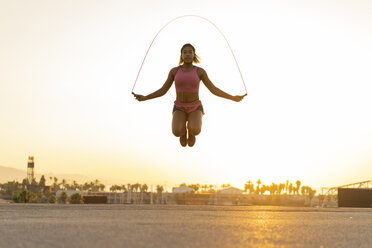 Spanien, Barcelona, junge schwarze Frau, die bei Sonnenaufgang Seil springt - AFVF01276