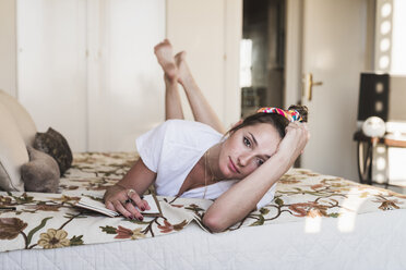 Portrait of young woman lying on bed at home with diary - KKAF01414