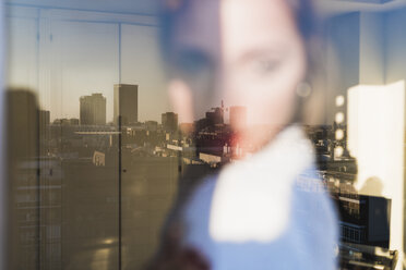 Spain, Madrid, blurred view of woman behind windowpane with reflection of the city - KKAF01419