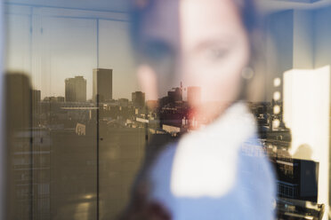 Spanien, Madrid, unscharfe Ansicht einer Frau hinter einer Fensterscheibe mit Spiegelung der Stadt - KKAF01419