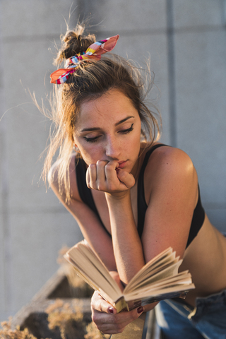 Junge Frau im BH, die auf dem Balkon ein Buch liest, lizenzfreies Stockfoto