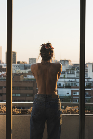 Rückansicht einer barbusigen jungen Frau auf einem Balkon, lizenzfreies Stockfoto