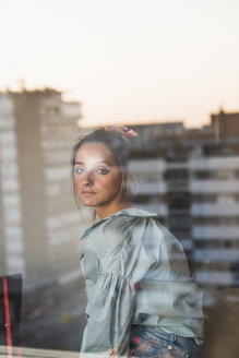 Porträt einer jungen Frau hinter einer Fensterscheibe mit Spiegelung der Stadt - KKAF01443