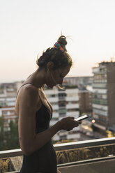 Young woman wearing black dress using cell phone on balcony - KKAF01451