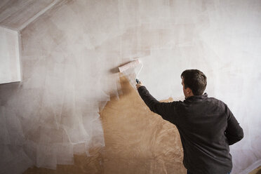 A builder, a painter holding a paint roll, painting a wall with white paint. - MINF05460