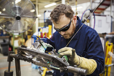 Männlicher Facharbeiter mit Schutzbrille beim Schweißen eines Fahrradteils in einer Fabrik. - MINF05474