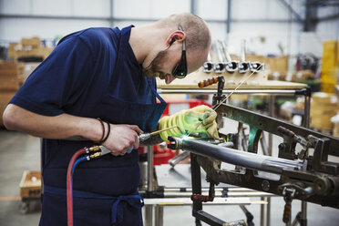 Männlicher Fabrikarbeiter schweißt Teile eines Fahrrads in einer Fabrik. - MINF05476