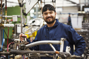 Male skilled factory worker with a partly assembled bicycle frame in a factory. - MINF05480