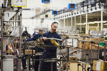 A man wearing one protective glove with sunglasses on his head, skilled factory worker working on bicycle parts in a factory. - MINF05481