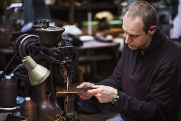 Ein Mann sitzt an einer großen Ledernähmaschine in einer Schuhmacherwerkstatt. - MINF05489