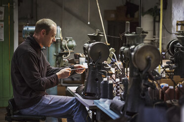 Man sitting at a sewing machine in a shoemaker's workshop. - MINF05490
