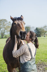 Woman standing outdoors, kissing a brown horse on the cheek. - MINF05501