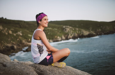 Sportive woman sitting on rocks in the evening - RAEF02079