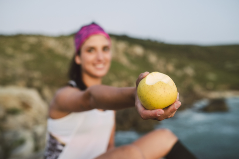 Sportive woman sitting on rocks, holding apple, focus on foreground stock photo