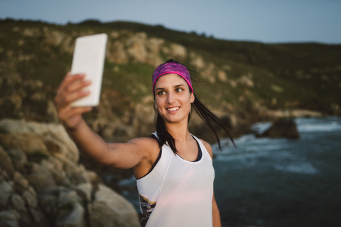 Sportliche Frau macht abends ein Selfie an der Küste, lizenzfreies Stockfoto