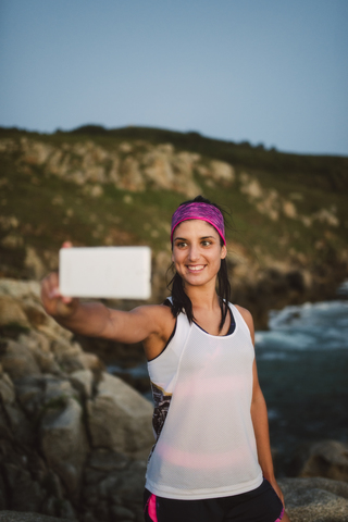 Sportliche Frau macht abends ein Selfie an der Küste, lizenzfreies Stockfoto