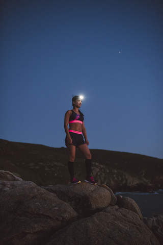 Sportive woman with headlamp standing on rocks in the evening stock photo