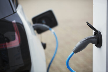 Electric car being charged with a cable connected to a wall socket. - MINF05528