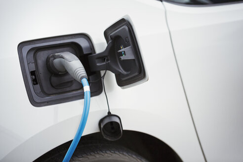 Nahaufnahme eines Elektroautos, das durch ein blaues Kabel aufgeladen wird, das an den Stecker angeschlossen ist und die Batterie auflädt. - MINF05529
