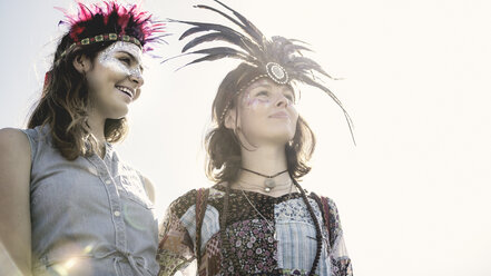 Zwei junge Frauen auf einem Sommermusikfestival mit bemalten Gesichtern und Federkopfschmuck. - MINF05554
