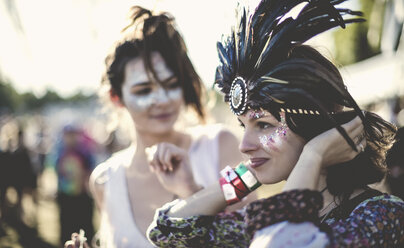 Two young women at a summer music festival faces painted, wearing feather headdress. - MINF05556