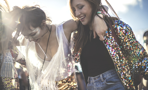 Two young women at a summer music festival wearing sequins with painted faces laughing and dancing. stock photo