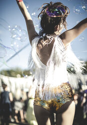 Rückansicht einer jungen Frau auf einem Sommermusikfestival, die goldene, mit Pailletten besetzte Hotpants trägt und in der Menge tanzt. - MINF05563