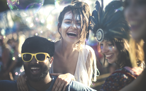 Revellers at a summer music festival young bearded man wearing yellow sunglasses and women with feather headdress and painted faces. stock photo