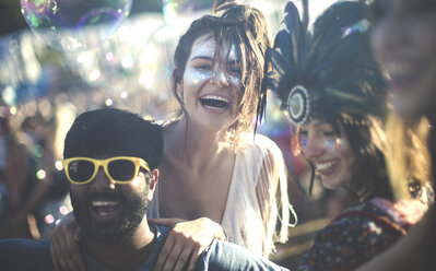 Nachtschwärmer auf einem Sommermusikfestival: junger bärtiger Mann mit gelber Sonnenbrille und Frauen mit Federkopfschmuck und bemalten Gesichtern. - MINF05568