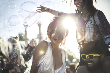 Ein junger Mann mit gelber Sonnenbrille, der eine Frau auf den Schultern trägt, feiert auf einem Musikfestival im Sommer. - MINF05569