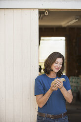 A woman holding a small fluffy chick, a baby bird in her two hands, standing at an open barn door. - MINF05584