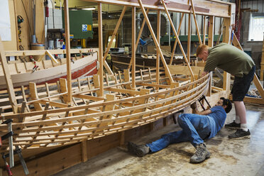 Zwei Männer in einer Bootsbauerwerkstatt, die gemeinsam an einem hölzernen Bootsrumpf arbeiten. - MINF05599