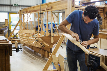 Mann in der Werkstatt eines Bootsbauers, der ein Holzruder bearbeitet. - MINF05605