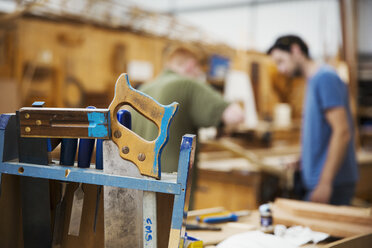 Nahaufnahme von Handwerkzeugen in der Werkstatt eines Bootsbauers, zwei Männer arbeiten im Hintergrund. - MINF05606